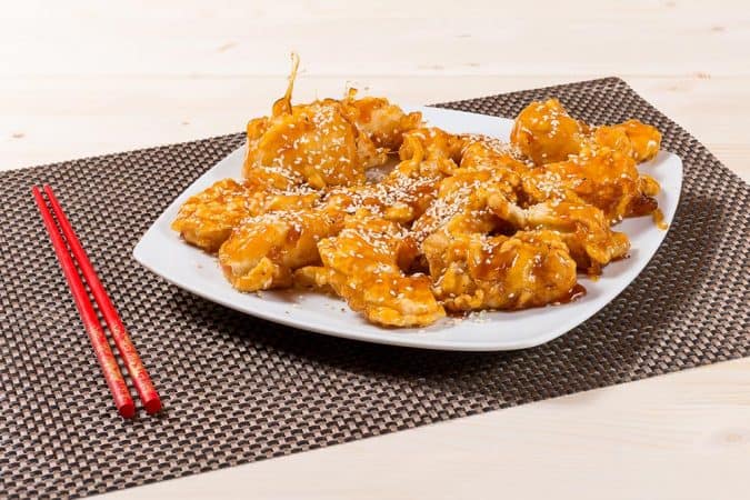 Pui prăjit crocant cu sos dulce-acrișor, servit pe o farfurie albă, specific bucătăriei chinezești.
