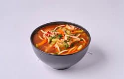 Ciorbă de pui aromată, servită într-un bol negru, cu legume și condimente proaspete.